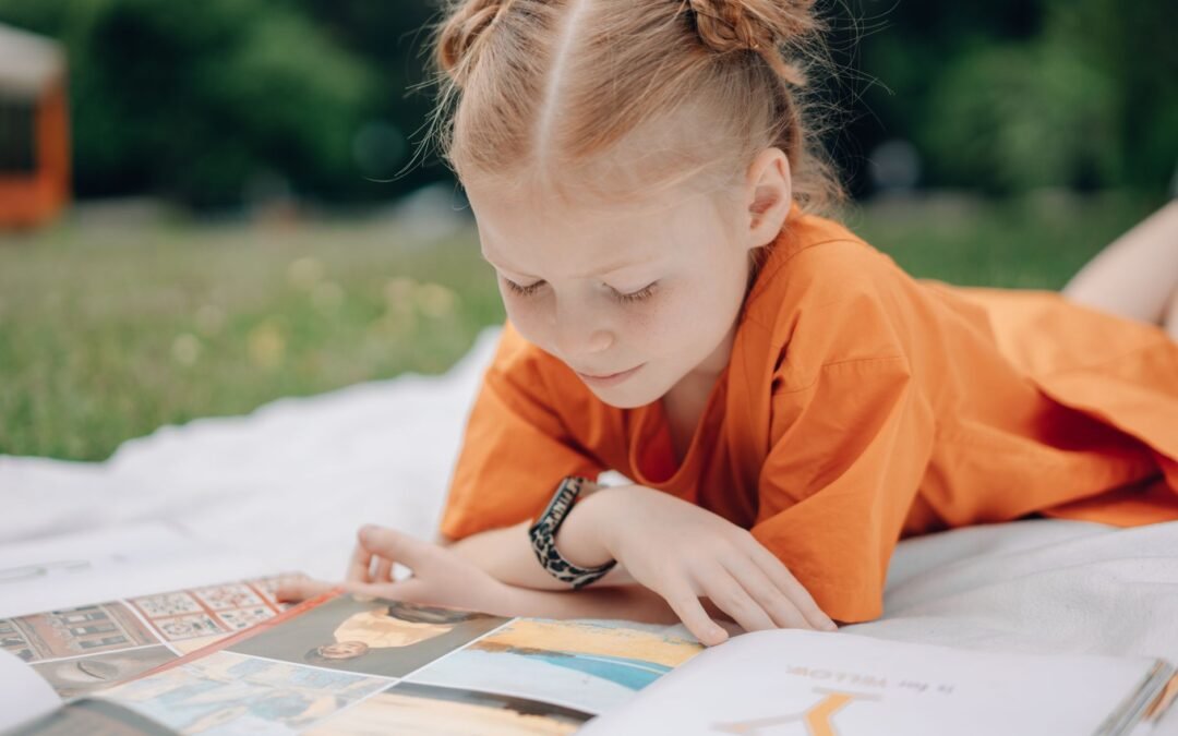a girl reading books on a blanket outdoors